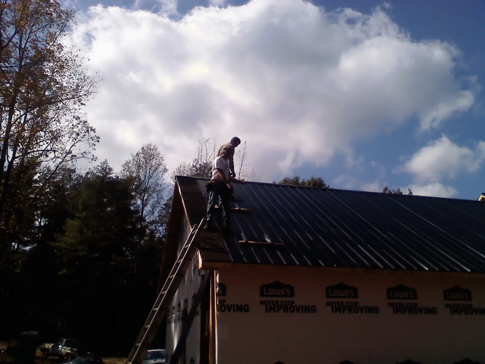 Roofer fastening dark metal panels high against a cloudy sky, from a Roof Inspection job in Fresno
